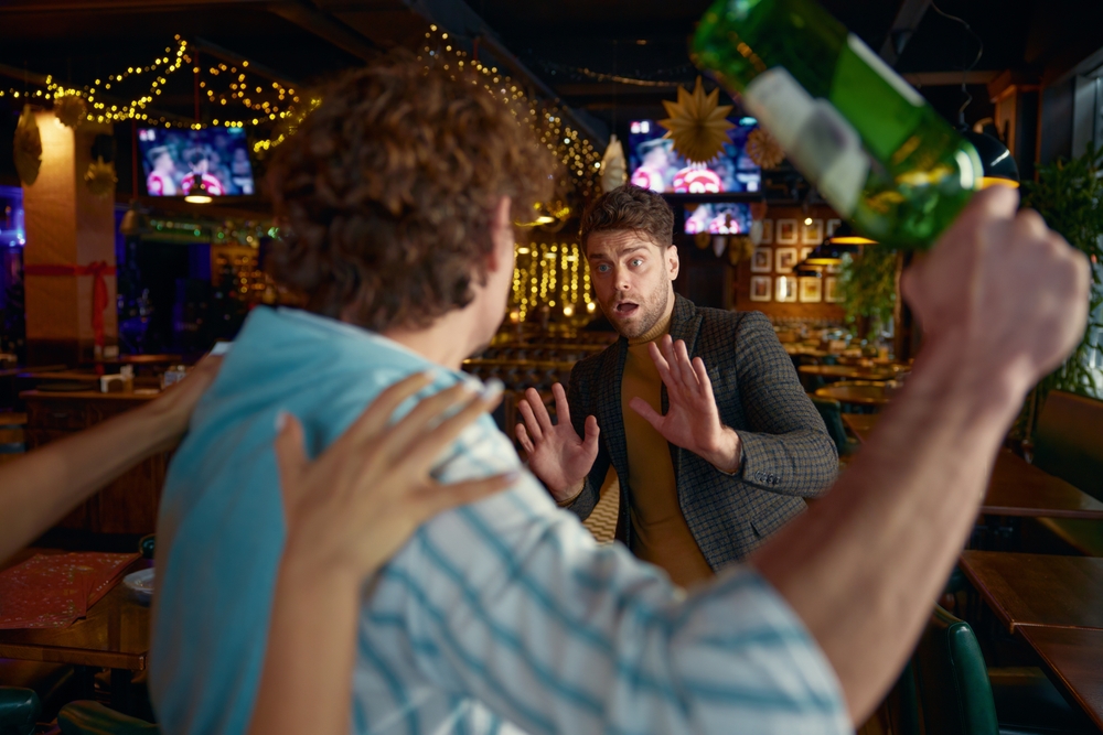 Man raising a bottle to strike another patron during a bar altercation while bystanders intervene